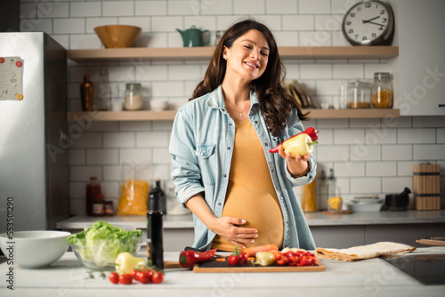 Obraz na plátně Young woman in kitchen. Beautiful pregnant woman making salad..