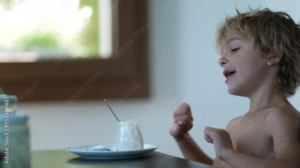 Candid kid stretching arms in morning after eating yogurt at breakfast