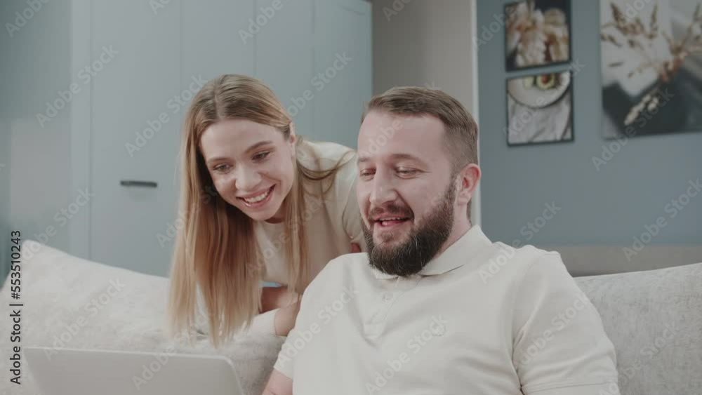 Video of happy beautiful couple using their laptop to searching voyage while she kisses him sitting on the couch at home. The story of one happy family. Video of happy beautiful couple using their laptop to searching voyage while she kisses him sitting on the couch at home. The story of one happy family.