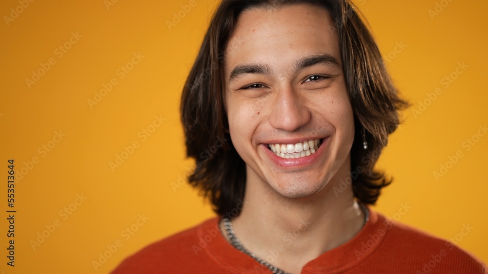 Closeup portrait of smiling Latino Hispanic gender fluid non-binary, young man 20s wearing orange shirt isolated on yellow color background in studio. Sincere emotions lifestyle concept. Closeup portrait of smiling Latino Hispanic gender fluid non-binary, young man 20s wearing orange shirt isolated on yellow color background in studio. Sincere emotions lifestyle concept.