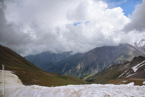Mountain range with peaks, thick clouds on the peaks, sunlight on the slopes, snow in the foreground, Chimbulak mountain resort, winter