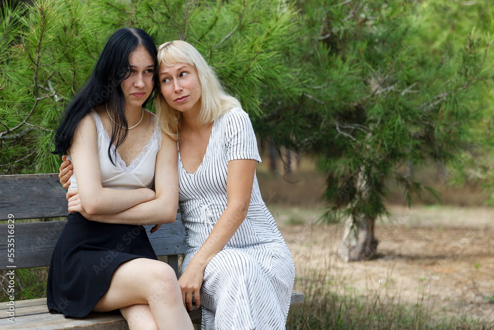 Attractive mid age mother and daughter sitting on a bench outdoors. Attractive mid age mother and daughter sitting on a bench outdoors.