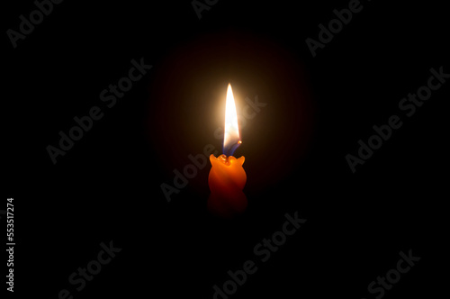 A single burning candle flame or light glowing on a beautiful spiral orange candle on black or dark background on table in church for Christmas, funeral or memorial service