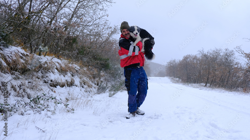 Hombre caucásico con un perro Border Collie en brazos en la nieve	