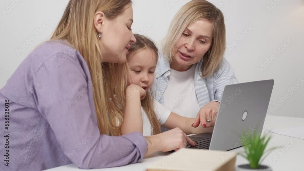 Working laptop. Little girl. Family education. Cute kid studying type laptop with mother and grandmother helping her sitting desk in light room interior.