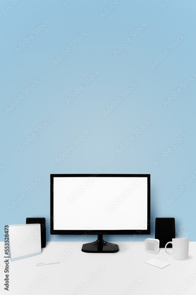 There is a monitor and office supplies on the desk in front of the blue wall. There is a monitor and office supplies on the desk in front of the blue wall.