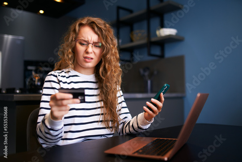 Worried woman with smartphone, debit card has problem paying bill, forgot banking app password. Female can't pay due to insufficient funds, sanctions, unsecure transfer. Unsuccessful transaction. photo