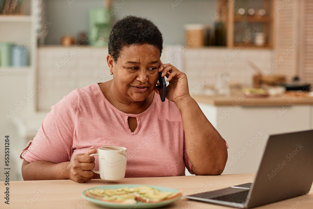 Warm toned portrait of black senior woman talking on phone while enjoying breakfast in morning Warm toned portrait of black senior woman talking on phone while enjoying breakfast in morning