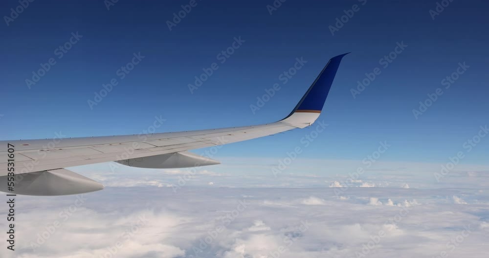 In background of fluffy cloudy sky, an airplane wing is seen flying above clouds skies from window In background of fluffy cloudy sky, an airplane wing is seen flying above clouds skies from window