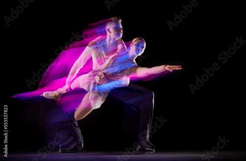 Portrait of artistic man and woman, figure skating athletes dancing isolated over black background in neon with mixed lights
