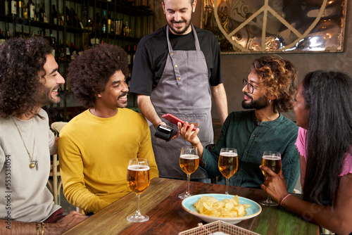 Customer making wireless or contactless payment using smartphone in a bar. Store worker accepting payment over NFC technology.