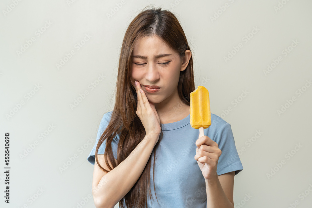 Face expression suffering from sensitive teeth and cold, asian young woman, girl feeling hurt, pain eating ice cream, lolly. Toothache molar tooth at home, dental problem isolated on white background. Face expression suffering from sensitive teeth and cold, asian young woman, girl feeling hurt, pain eating ice cream, lolly. Toothache molar tooth at home, dental problem isolated on white background.