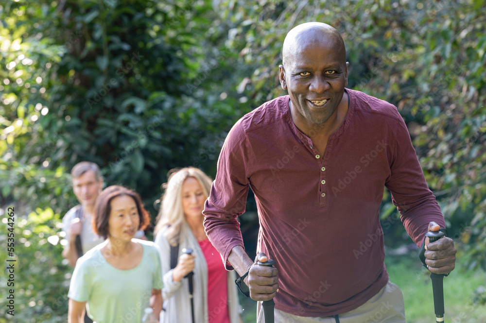 Senior African-American man holding hiking poles going for a hike with group of diverse senior friends Senior African-American man holding hiking poles going for a hike with group of diverse senior friends