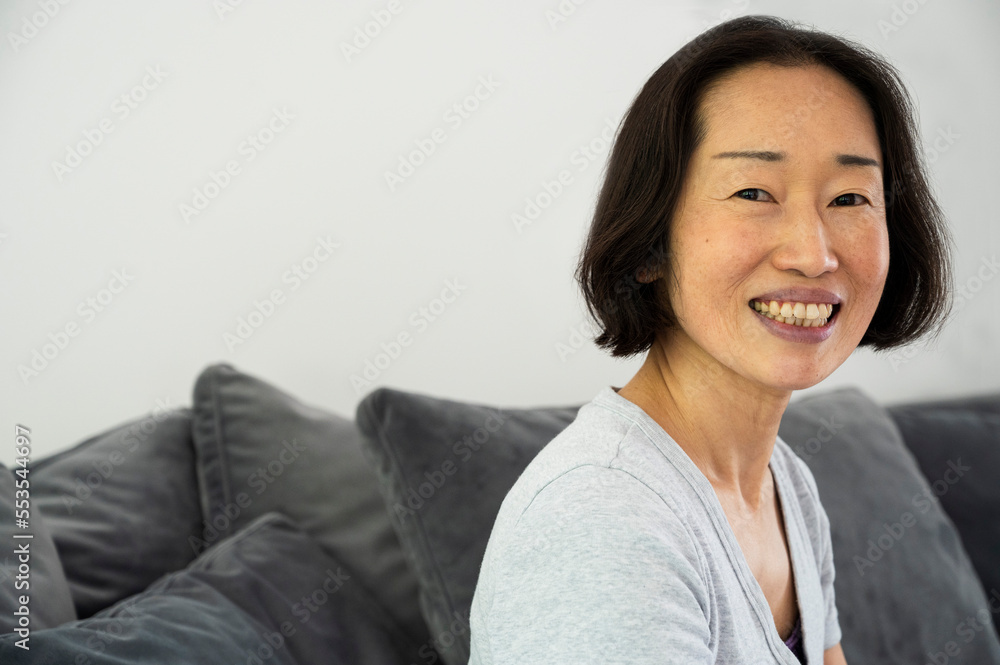 Portrait of Asian-American senior woman smiling and looking at camera while sitting in living room Portrait of Asian-American senior woman smiling and looking at camera while sitting in living room