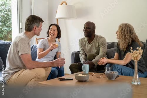 Group of senior friends sitting on sofa while drinking juice and tea