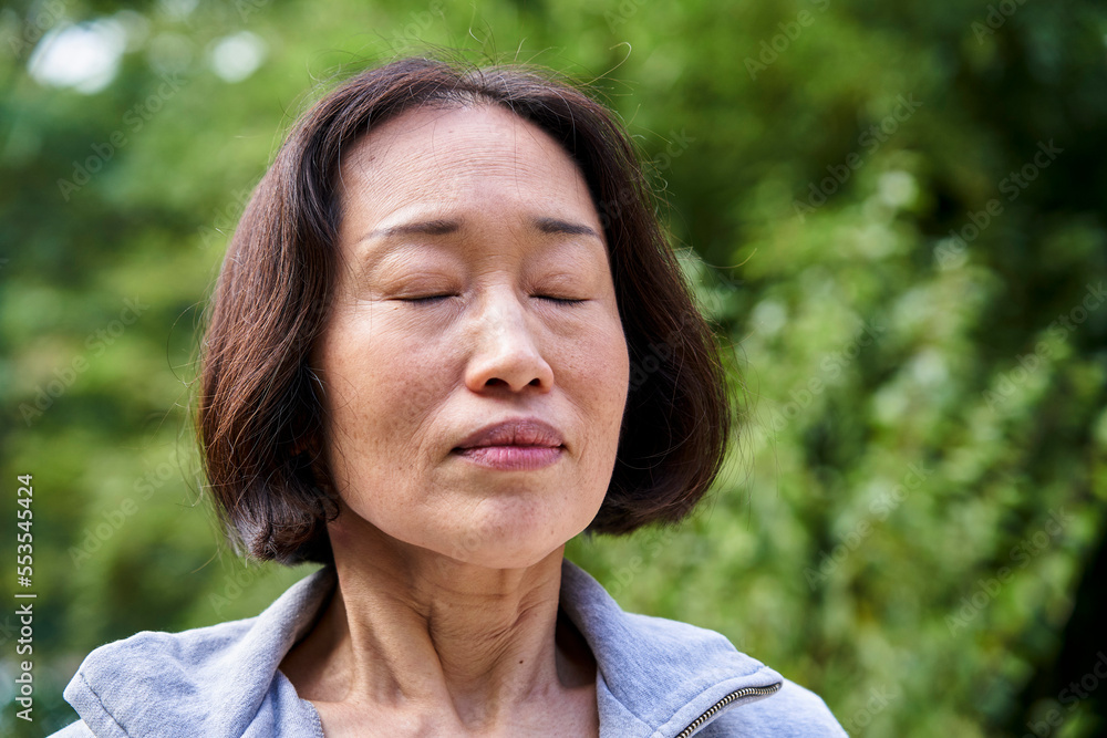 Senior Asian woman with eyes closed standing indoors Senior Asian woman with eyes closed standing indoors