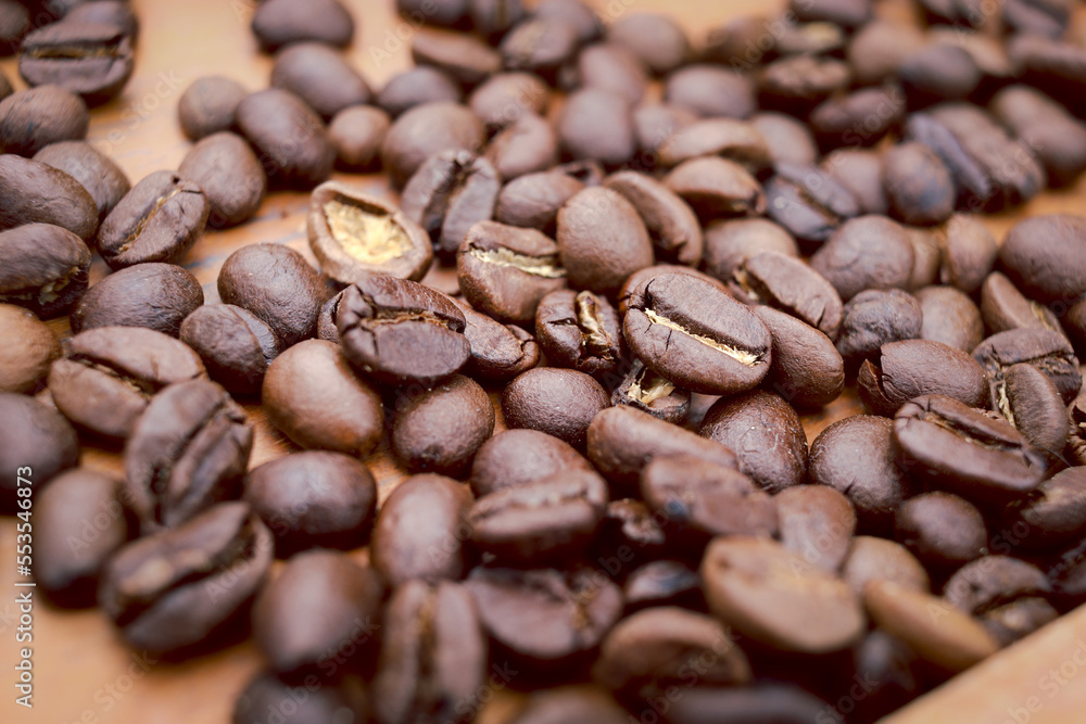 Naklejka premium Roasted dark brown coffee beans on top of the wooden table, closeup coffee seeds background