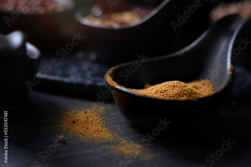 Spices and herbs on dark background, yellow turmeric powderin tablespoon with assorted colorful of seasoning ingredients as blurred background photo