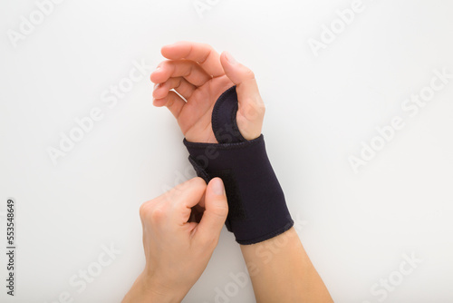 Young adult woman hand putting protective black elastic wrist bandage on white table background. Closeup. Point of view shot. Top down view. photo