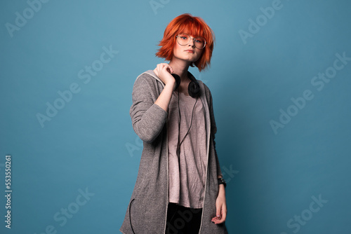 Portrait of stylish teenage girl with makeup in headphones on blue background.