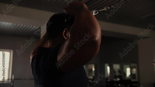 Black Man workout in the gym doing shoulder exercise in crossover.Bodybuilder training back delts with cable equipment indoors.Training concept with rope cable. 