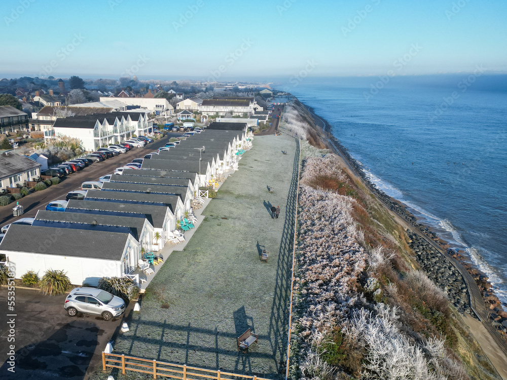 Obraz premium Aerial view of holiday chalets seen on the Suffolk coast during early winter. A couple can be seen out for an early stroll with the North Sea in view.