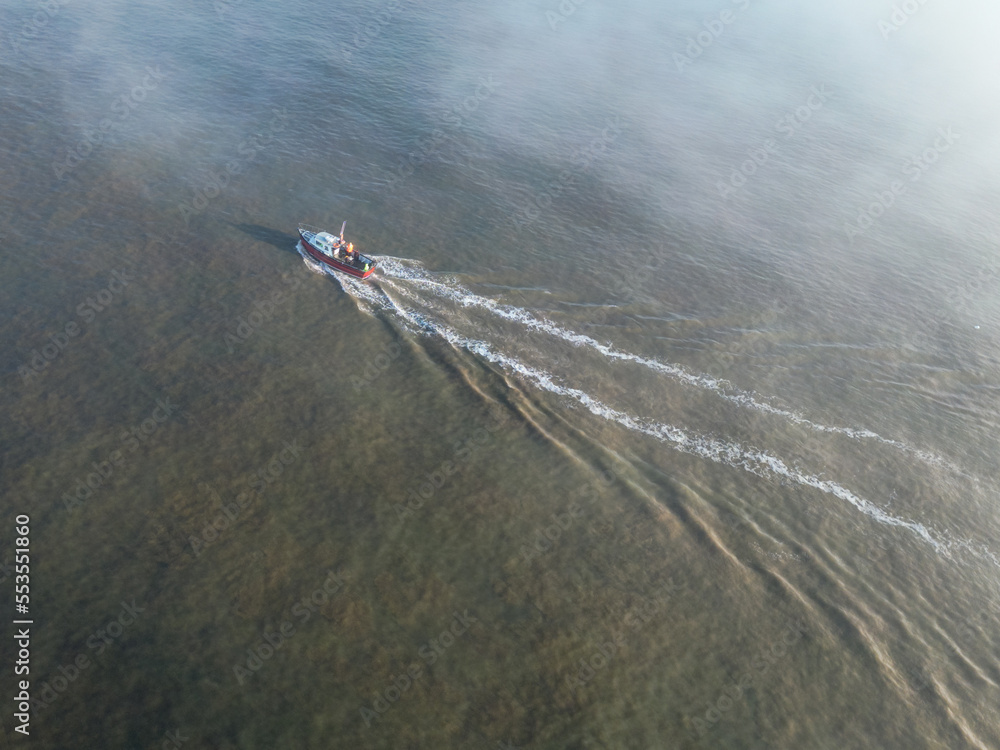 Naklejka premium Aerial view of a small pleasure fishing boat with sea anglers on board. A dense fog bank is starting the engulf the area and is causing a hazard to shipping.