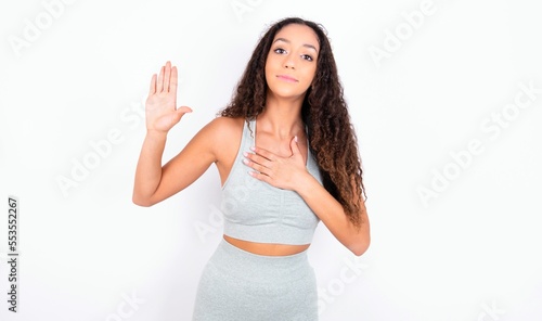 teen girl with curly hair wearing white sport set over gray background Swearing with hand on chest and open palm, making a loyalty promise oath photo