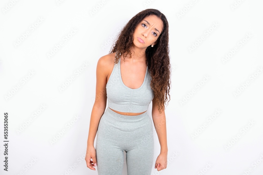 Displeased upset Beautiful teen girl with curly hair wearing grey sport set frowns face as going to cry, being discontent and unhappy as can't achieve goals, Disappointed model has troubles Displeased upset Beautiful teen girl with curly hair wearing grey sport set frowns face as going to cry, being discontent and unhappy as can't achieve goals, Disappointed model has troubles