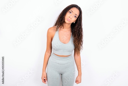 Displeased upset Beautiful teen girl with curly hair wearing grey sport set frowns face as going to cry, being discontent and unhappy as can't achieve goals,  Disappointed model has troubles © Roquillo
