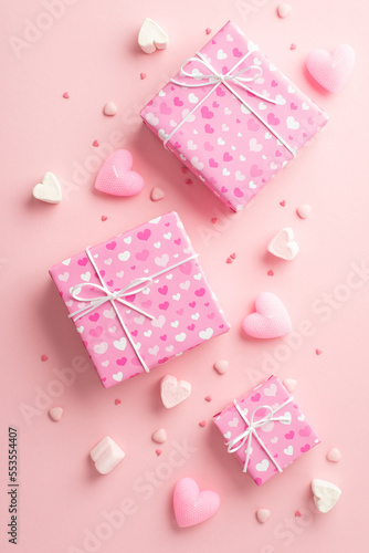 Valentine's Day concept. Top view vertical photo of gift boxes in wrapping paper with heart pattern candles marshmallow and sprinkles on isolated pastel pink background © ActionGP