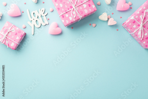 Valentine's Day concept. Top view photo of pink gift boxes in wrapping paper with heart pattern marshmallow candles inscription love you and sprinkles on isolated pastel blue background with copyspace