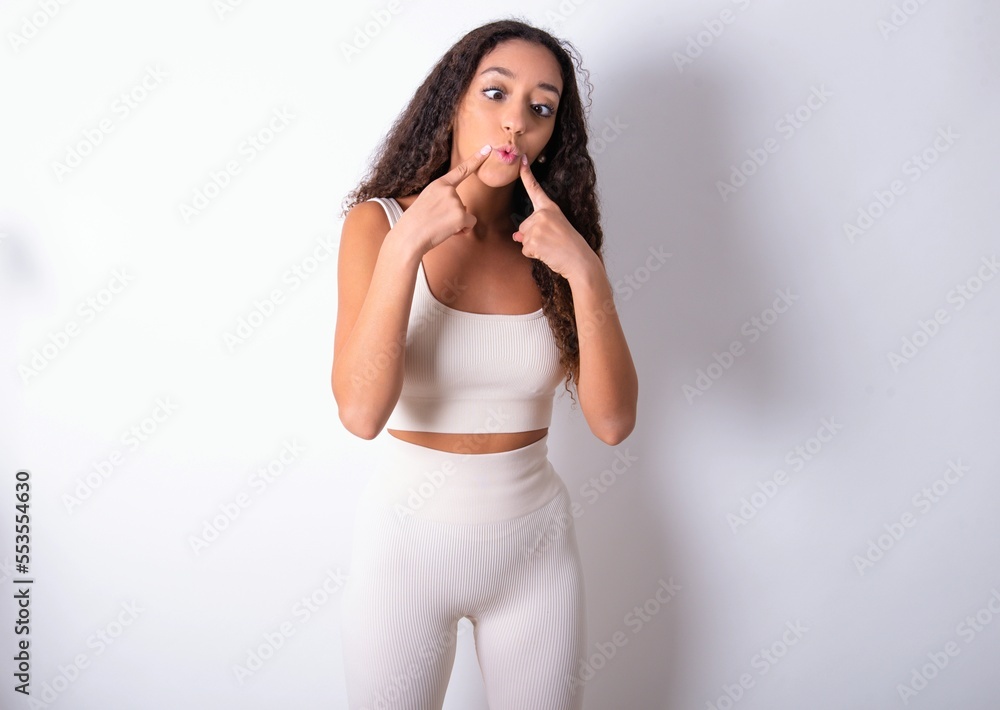teen girl with curly hair wearing white sport set over white background crosses eyes and makes fish lips funny grimace teen girl with curly hair wearing white sport set over white background crosses eyes and makes fish lips funny grimace