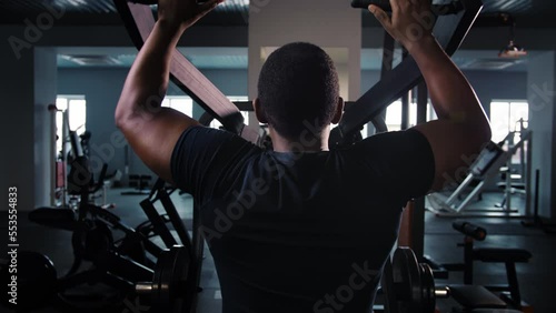 Black man training back muscle doing pulls weight exercise in a gym.Athlete do workout in simulator machine new equipment.Bodybuilder pumping back sitting on gym machine.