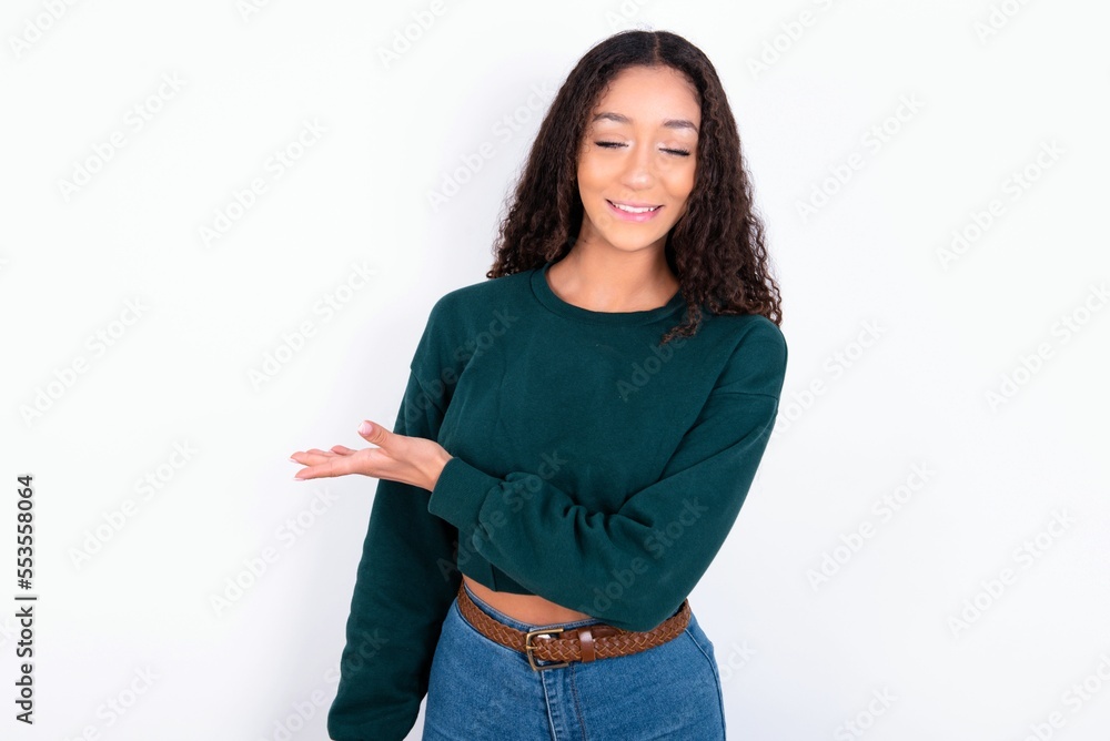teen girl wearing knitted green sweater over white background says: wow how exciting it is, has amazed expression, shows something on blank space with palm. Advertisement concept. teen girl wearing knitted green sweater over white background says: wow how exciting it is, has amazed expression, shows something on blank space with palm. Advertisement concept.