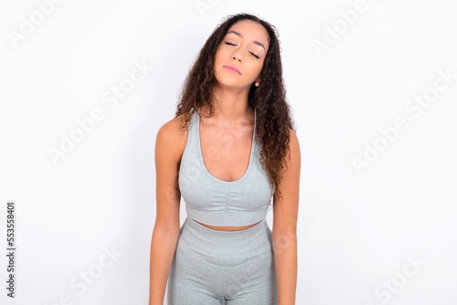 teen girl with curly hair wearing white sport set over gray background looking sleepy and tired, exhausted for fatigue and hangover, lazy eyes in the morning.