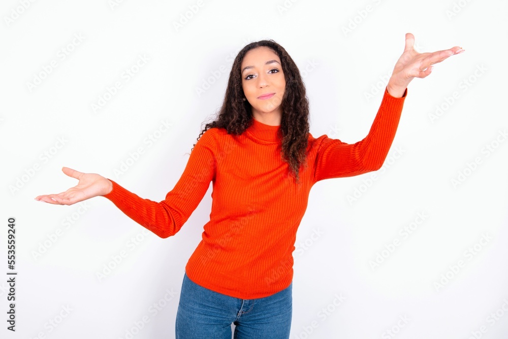 Cheerful teen girl wearing knitted red sweater over white background making a welcome gesture raising arms over head. Cheerful teen girl wearing knitted red sweater over white background making a welcome gesture raising arms over head.