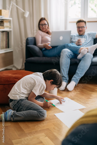 Boy draws on the floor and his parents are watching him