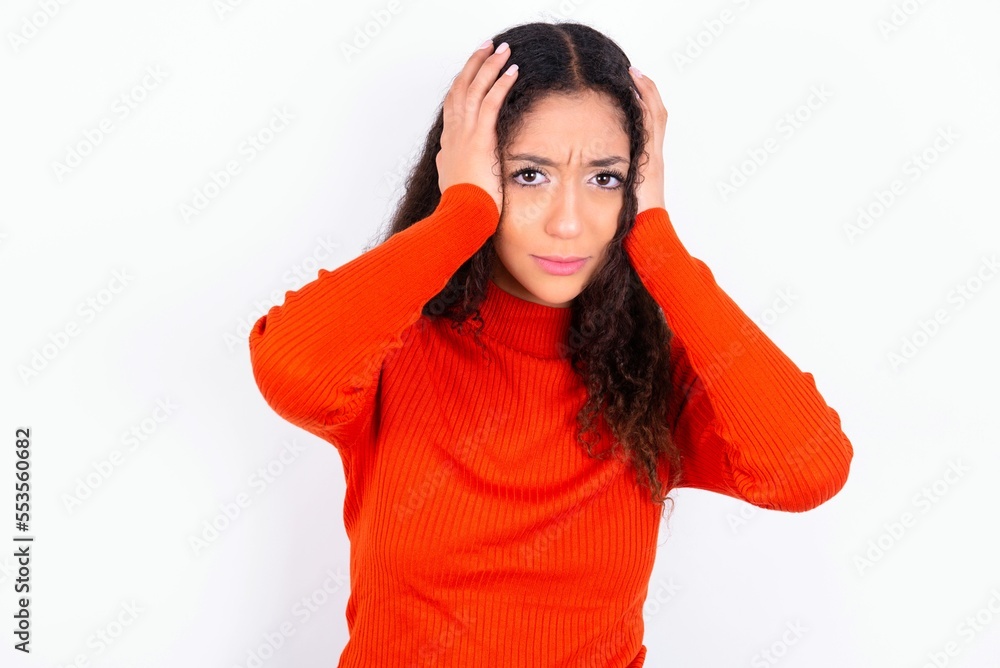 teen girl wearing knitted red sweater over white background holding head in hands with unhappy expression watching sad movie about animals and trying not to cry. teen girl wearing knitted red sweater over white background holding head in hands with unhappy expression watching sad movie about animals and trying not to cry.