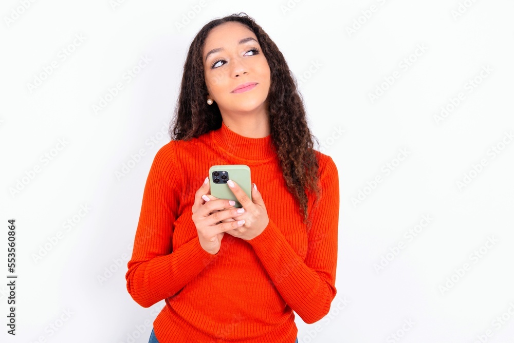 Happy teen girl wearing knitted red sweater over white background listening to music with earphones using mobile phone. Happy teen girl wearing knitted red sweater over white background listening to music with earphones using mobile phone.