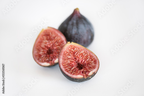 Isolated Black mission figs, one whole and one halved, positioned on a bright surface showing seeds, pulp and skin, edible delicious fruit consumed fresh or used as ingredient in Mediterranean cuisine