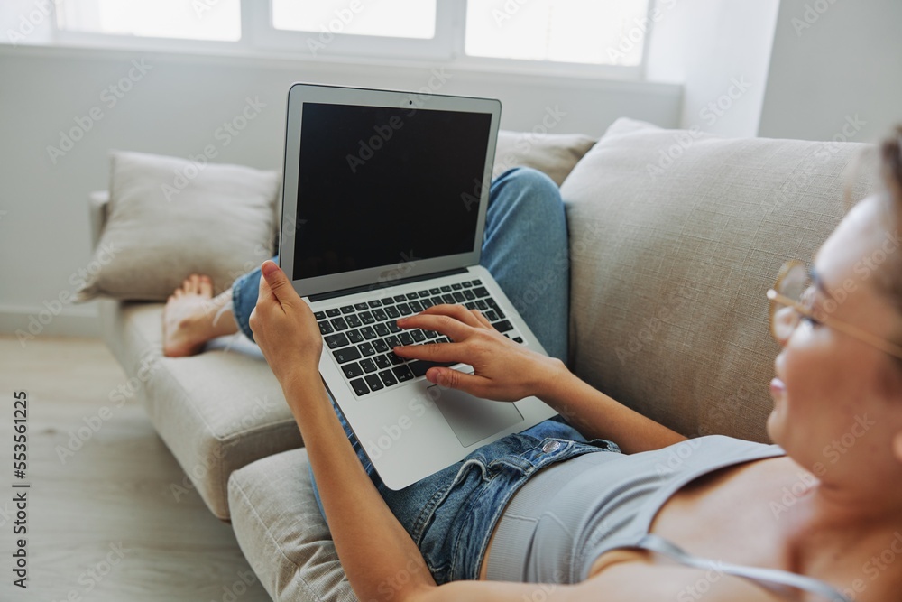 Fototapeta premium Teenage girl freelancer with laptop sitting on couch at home smiling in home clothes and glasses with short haircut, lifestyle with no filters, free copy space