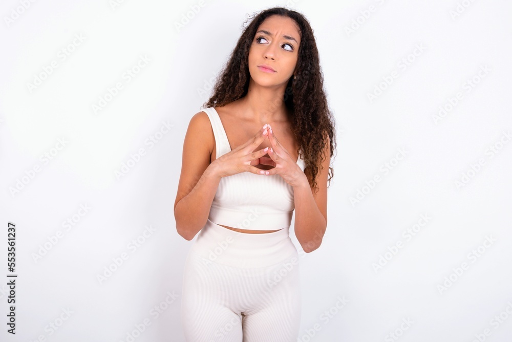 teen girl with curly hair wearing white sport set over white background steepled fingers and looks mysterious aside has great evil plan in mind teen girl with curly hair wearing white sport set over white background steepled fingers and looks mysterious aside has great evil plan in mind