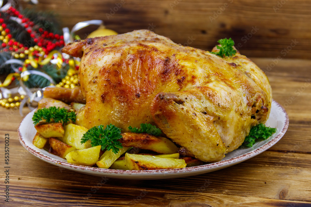 Baked whole chicken with potato and Christmas decorations on a wooden table Baked whole chicken with potato and Christmas decorations on a wooden table