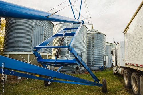 An auger assembly and grain truck parked beside silos in a farmyard; Legal, Alberta, Canada