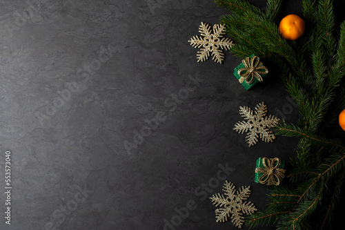 Dark christmas background with green fir branch,  gift boxes and tangerines, place for text photo