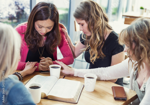 A group of women gathered together praying for one of the women after a Bible study in a coffee shop at a church; Edmonton, Alberta, Canada