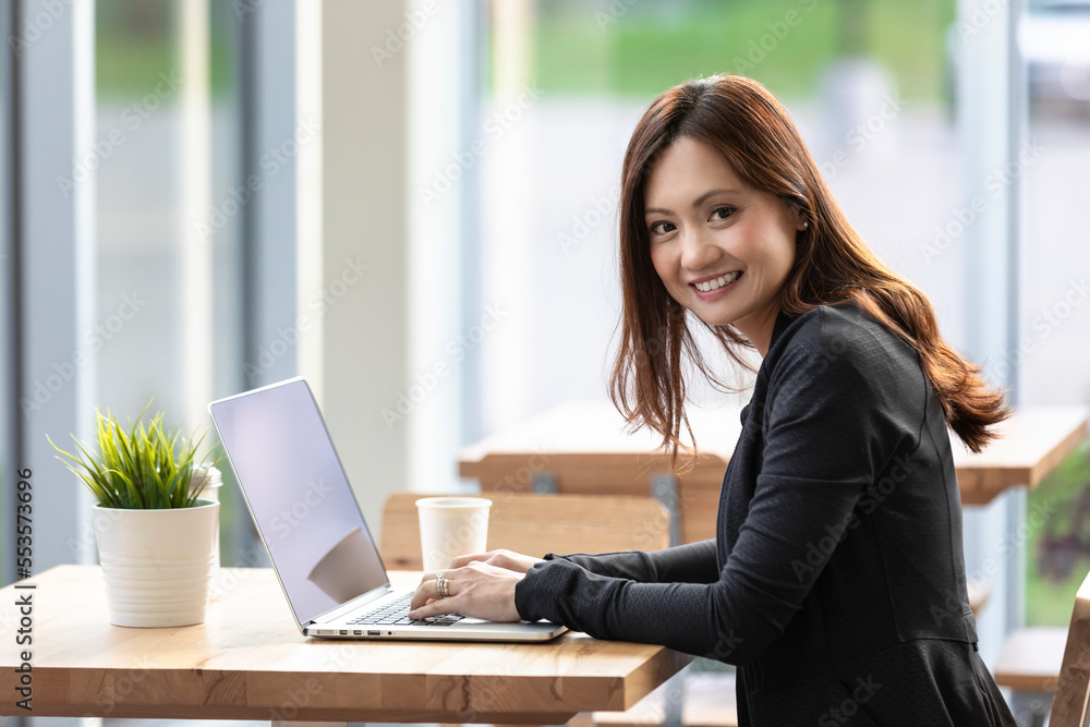 A professional Asian woman working on a computer in a coffee shop and stopping to look at the camera: Edmonton, Alberta, Canada