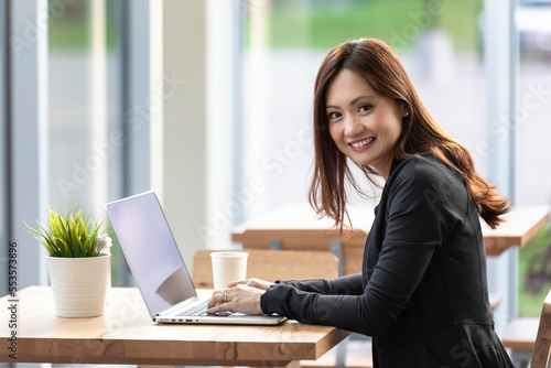 A professional Asian woman working on a computer in a coffee shop and stopping to look at the camera: Edmonton, Alberta, Canada photo