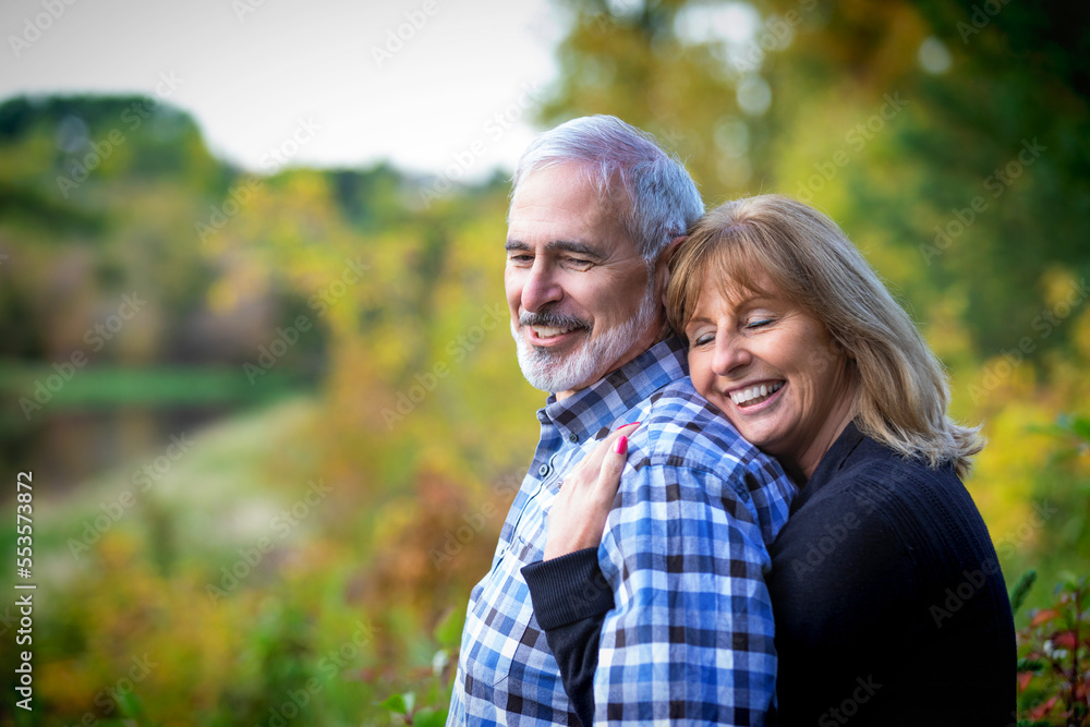 A mature couple enjoying time together and enjoying the sunset along a river in a city park on a warm fall evening; St. Albert, Alberta, Canada A mature couple enjoying time together and enjoying the sunset along a river in a city park on a warm fall evening; St. Albert, Alberta, Canada